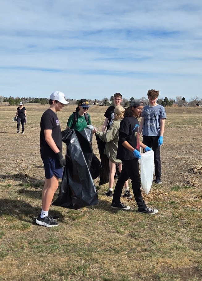 Students picking up trash in an open field while wearing gloves and carrying bags.