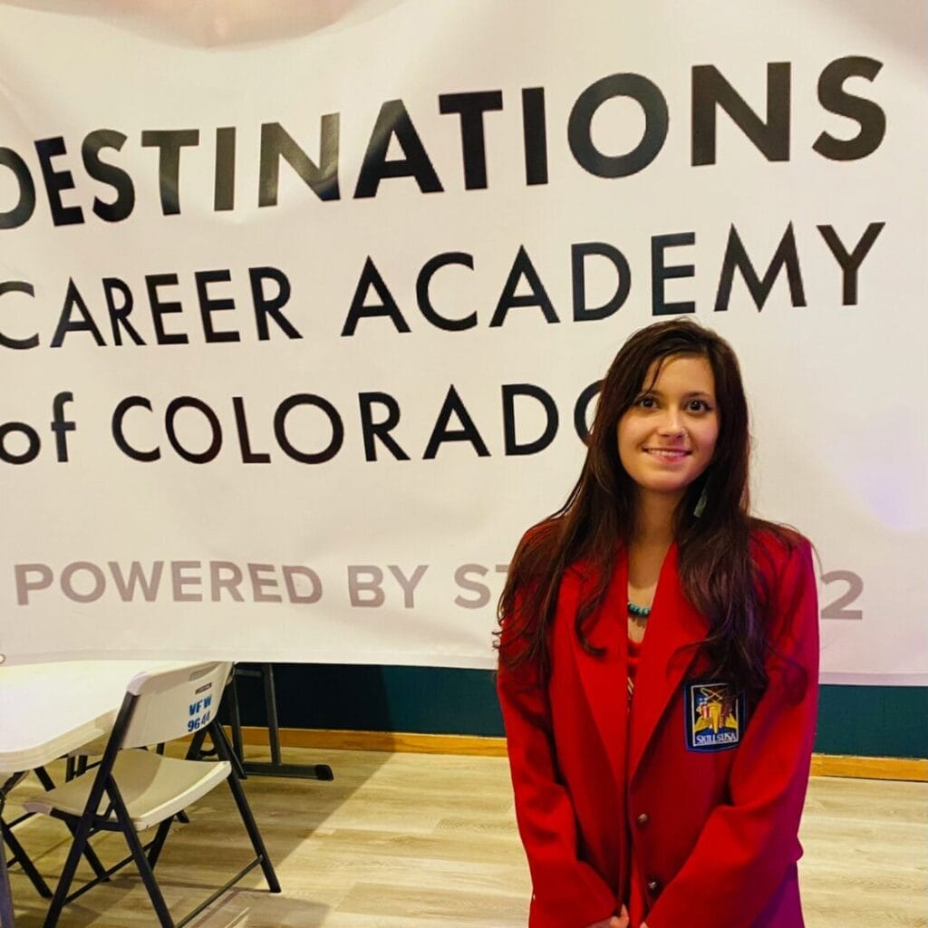 Student smiling in front of a Destinations Career Academy of Colorado Banner.