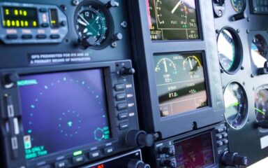 Aircraft cockpit panel with various digital screens, gauges, and control knobs.
