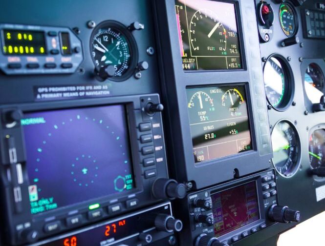 Aircraft cockpit panel with various digital screens, gauges, and control knobs.