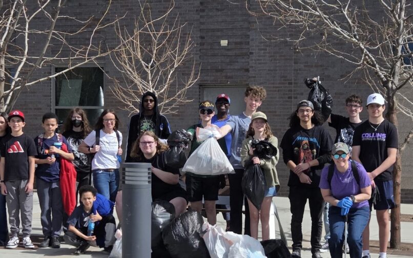 A group of students standing outdoors holding trash bags during a community cleanup.